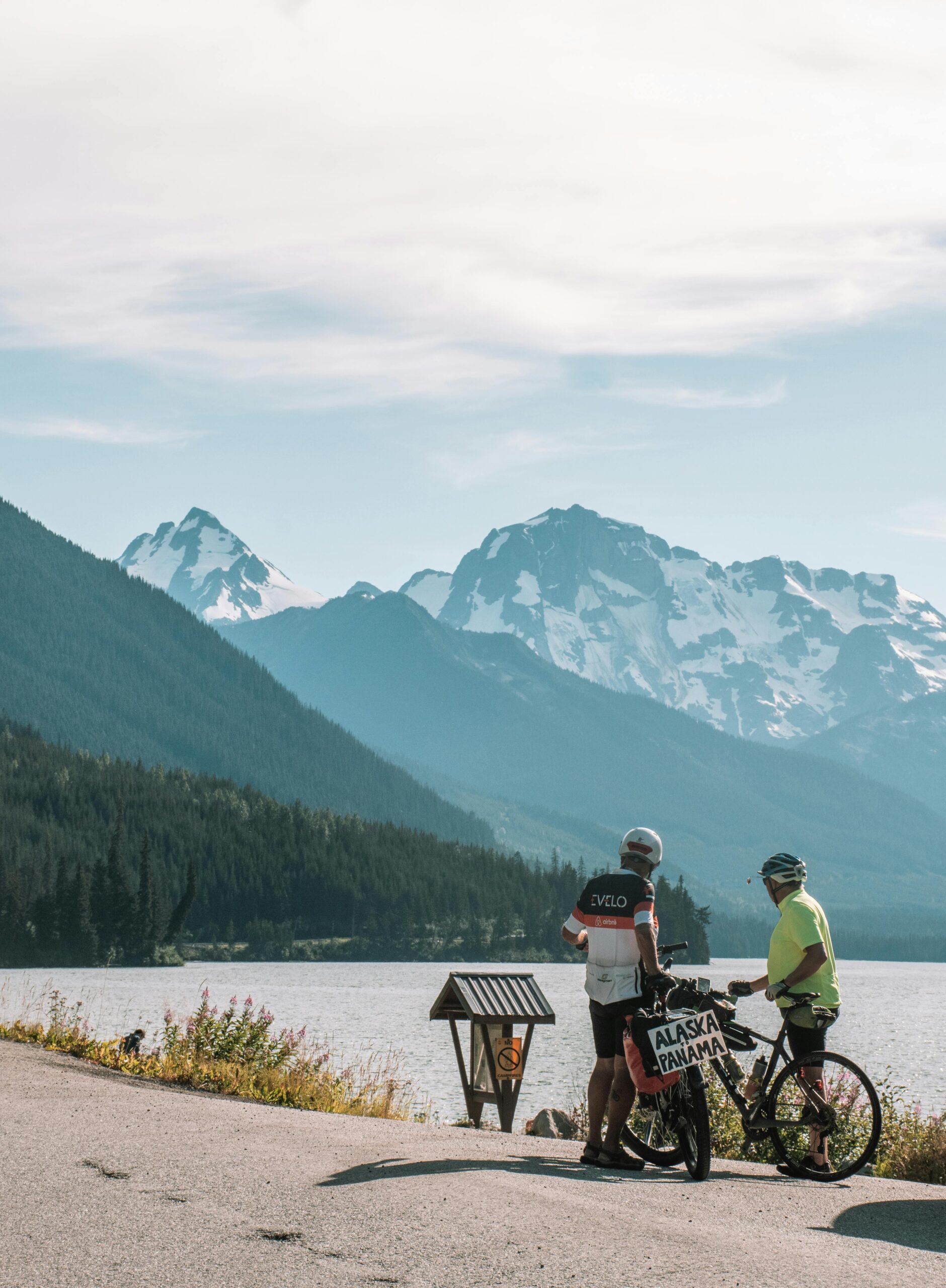Two people on bikes near a lake with mountains in the background